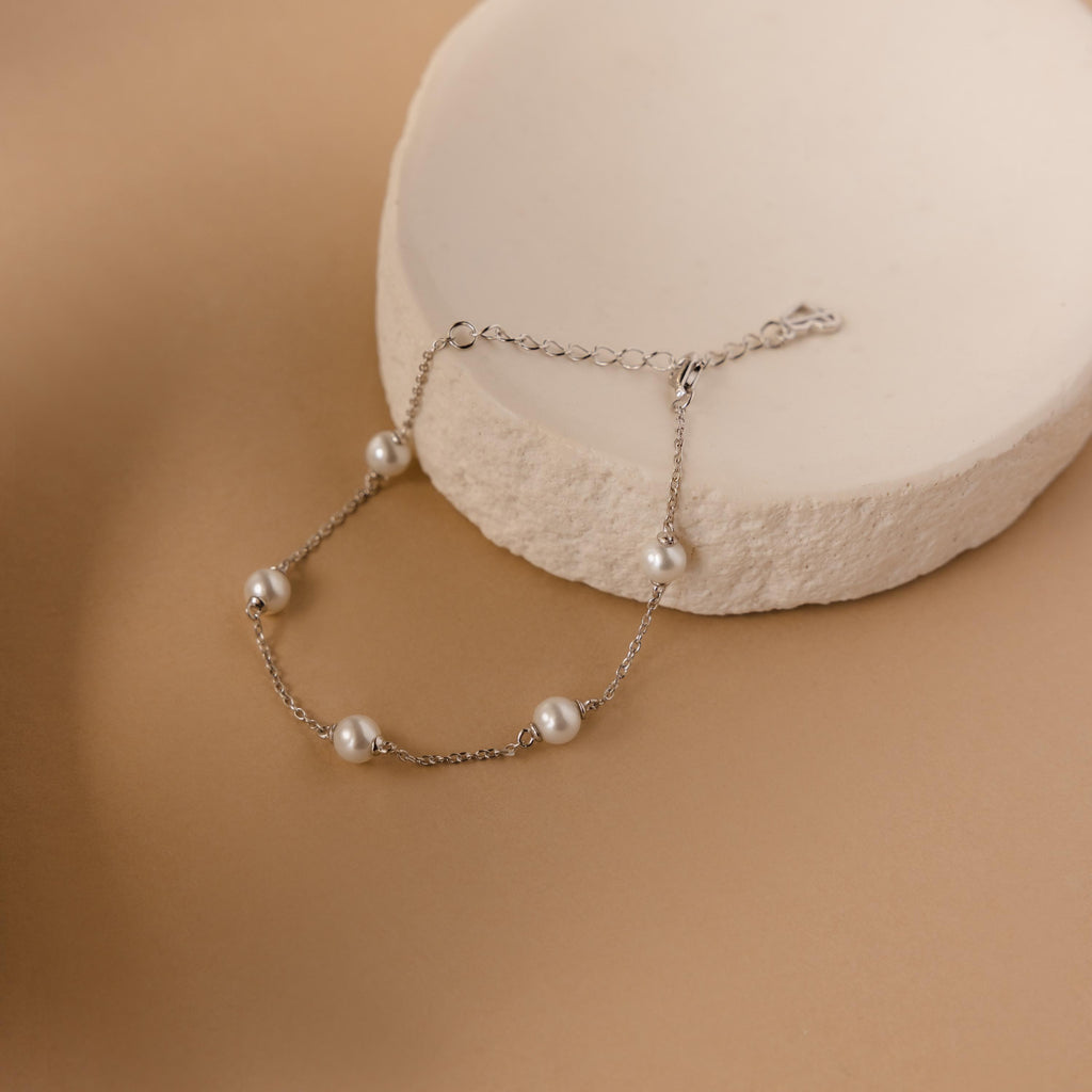 The Pearl Station Bracelet in Sterling Silver features five pearls on a round, textured off-white platform—a chic accessory for any occasion.