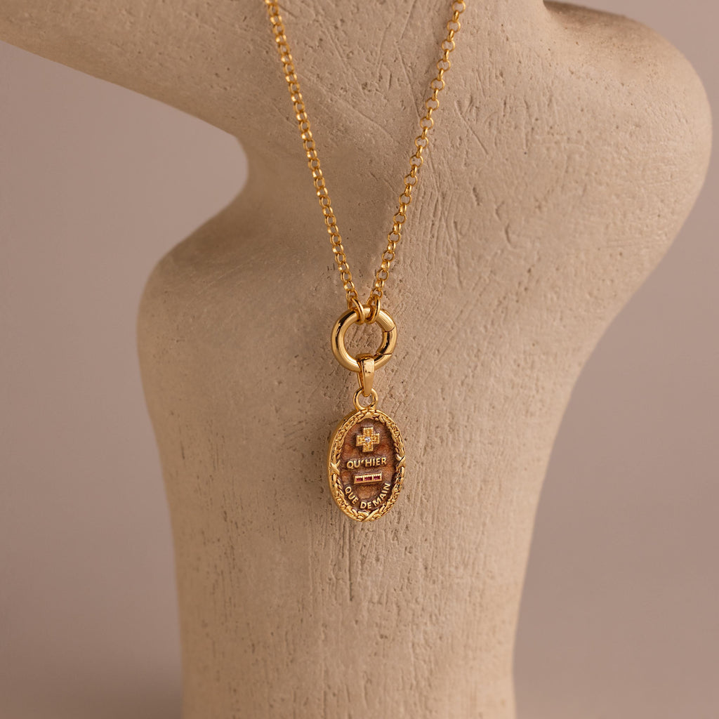 The Love Poem Pendant Necklace features engraved details and is showcased on a beige textured stand with a neutral background—a timeless love token.