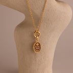 The Love Poem Pendant Necklace features engraved details and is showcased on a beige textured stand with a neutral background—a timeless love token.