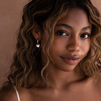 A woman with wavy hair wears Mixed Metal Heart Huggies, gazing at the camera with a gentle smile.