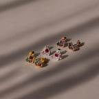 Five pairs of Mixed Birthstone Heart Studs lie on a neutral surface, their customizable gemstones reflecting soft shadows.