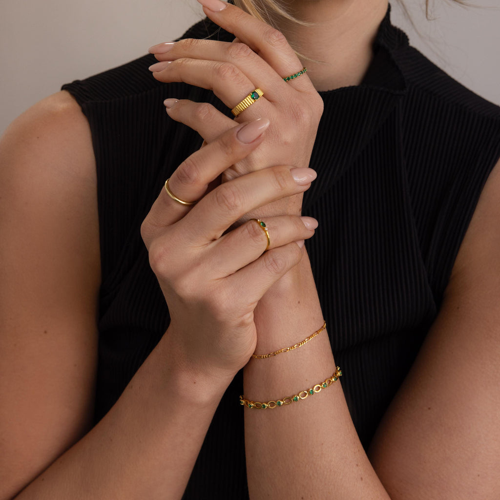 A woman in a black top displays her hands adorned with gold rings and the Emerald Chain Tennis Bracelet.