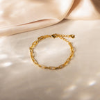 The Pave Paperclip Chain Bracelet features rectangular links with small crystals, elegantly displayed on a soft beige fabric background.