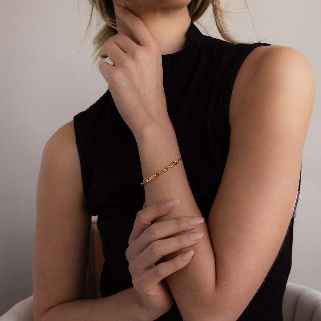 Woman in a sleeveless black top wears the Pave Paperclip Chain Bracelet, elegantly touching her chin with one hand.