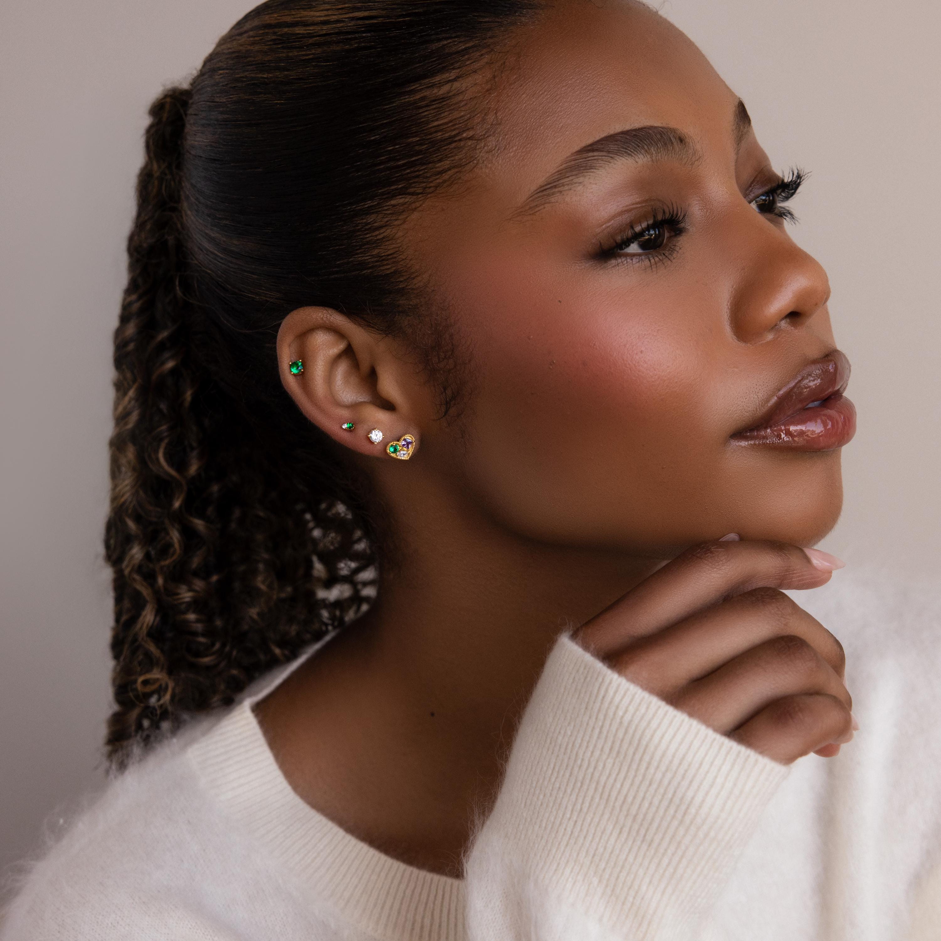 A woman with her hand on her chin, displaying Mixed Birthstone Heart Studs—elegant earrings featuring customizable gemstones.