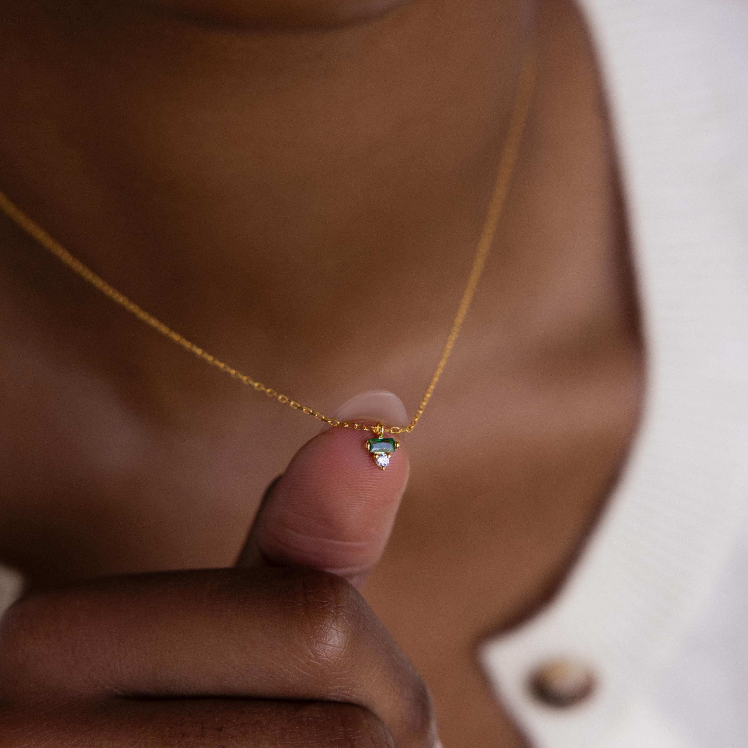 Close-up of a hand holding the Baguette Birthstone Drop Necklace with a small heart-shaped pendant against the chest.