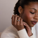 A woman with closed eyes gently touches her face, displaying the elegant Mixed Birthstone Dome Ring on her finger.