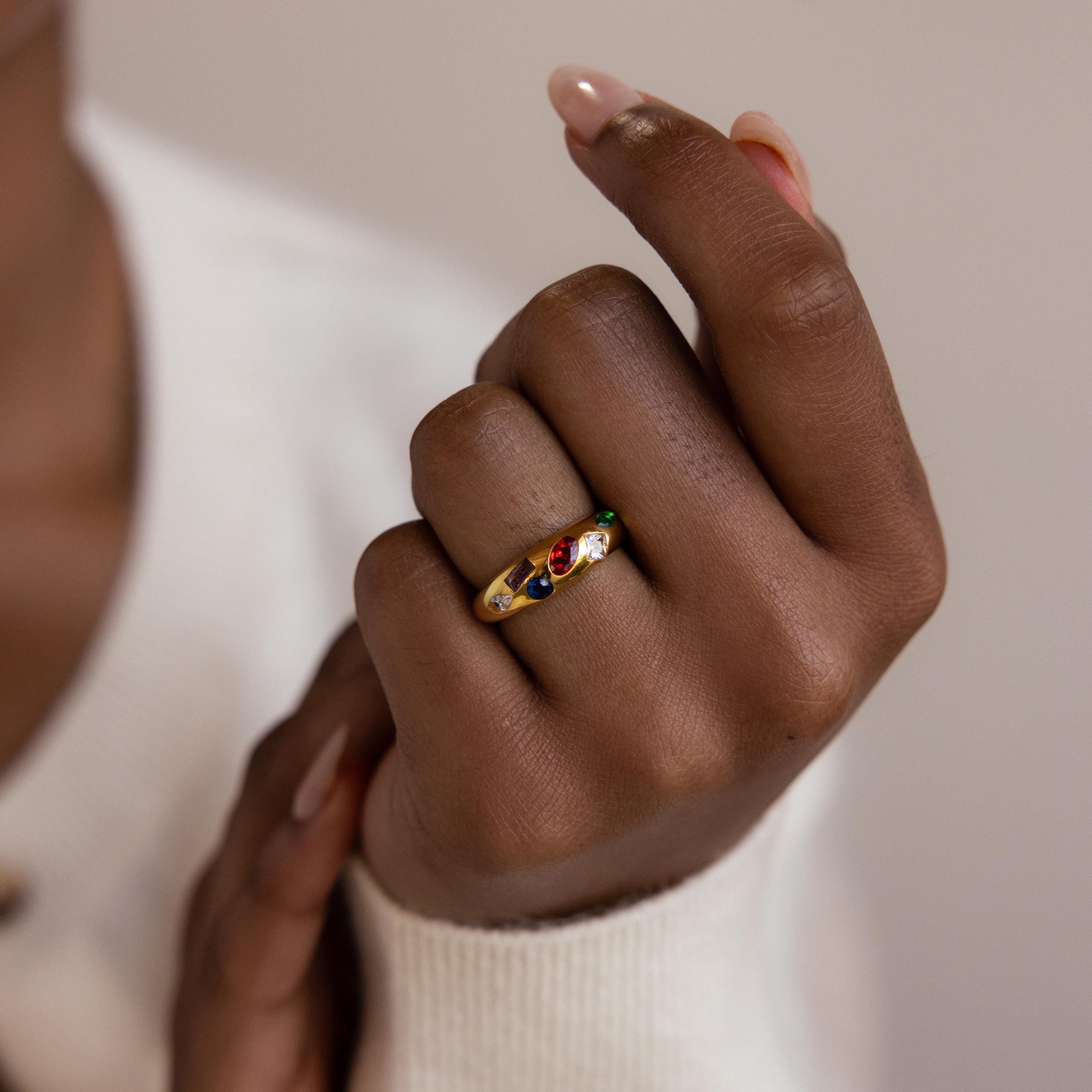 A hand wearing the Mixed Birthstone Dome Ring, a gold customizable ring set with vibrant gemstones, shown against a neutral background.