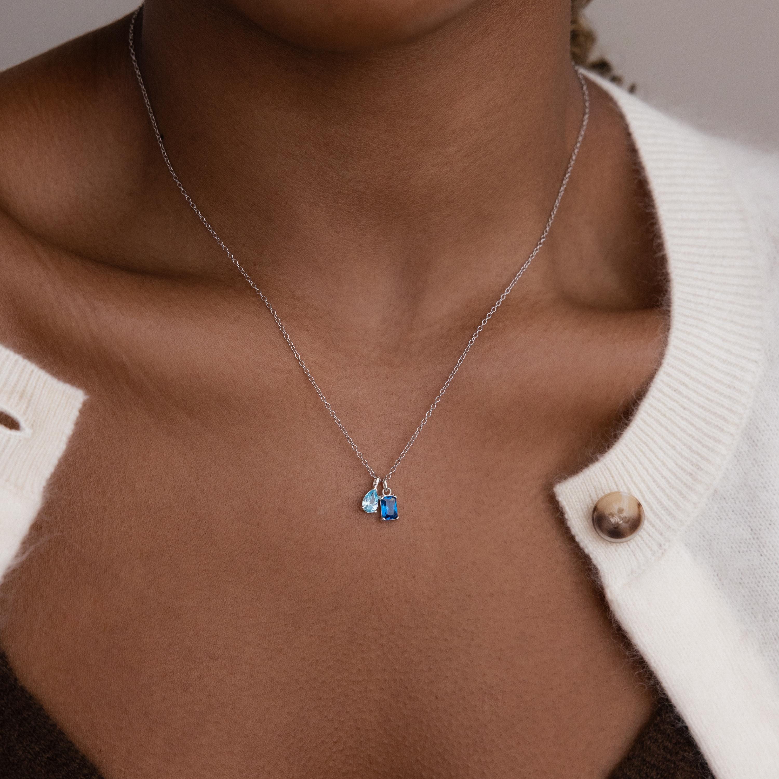 Model wears silver cable chain with aquamarine pear birthstone charm and blue zircon baguette birthstone charm