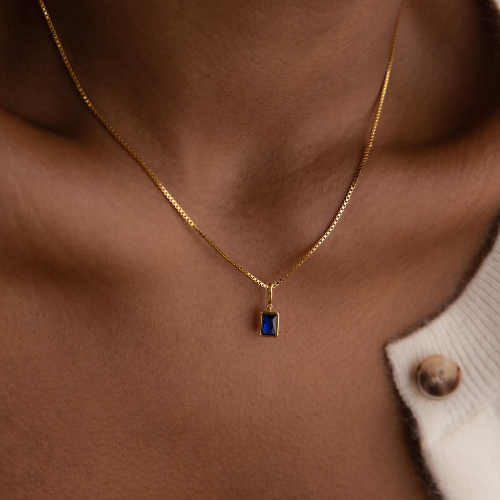 Model wears a box chain with a dangling gold Sapphire Emerald-cut Charm