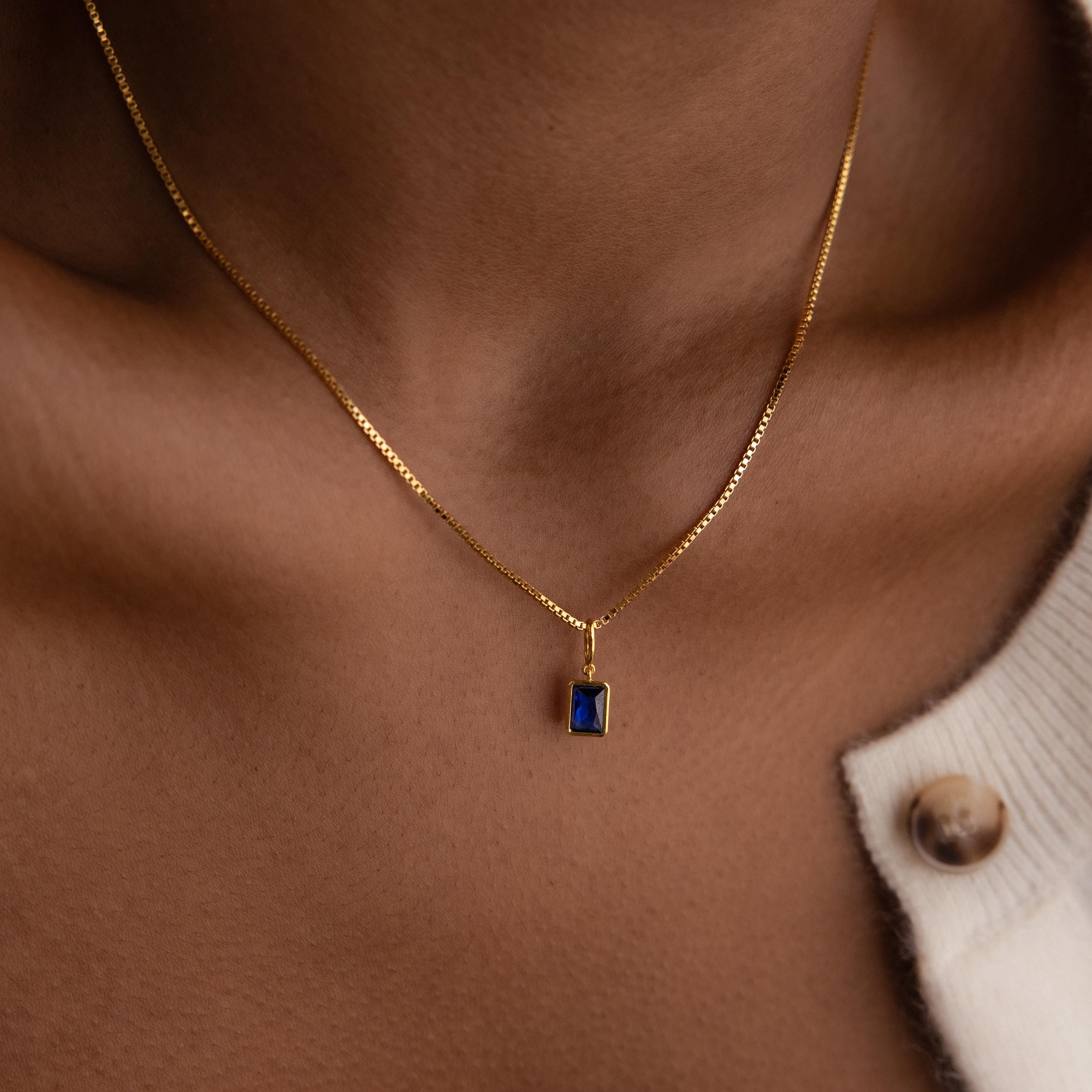 Model wears a box chain with a dangling gold Sapphire Emerald-cut Charm