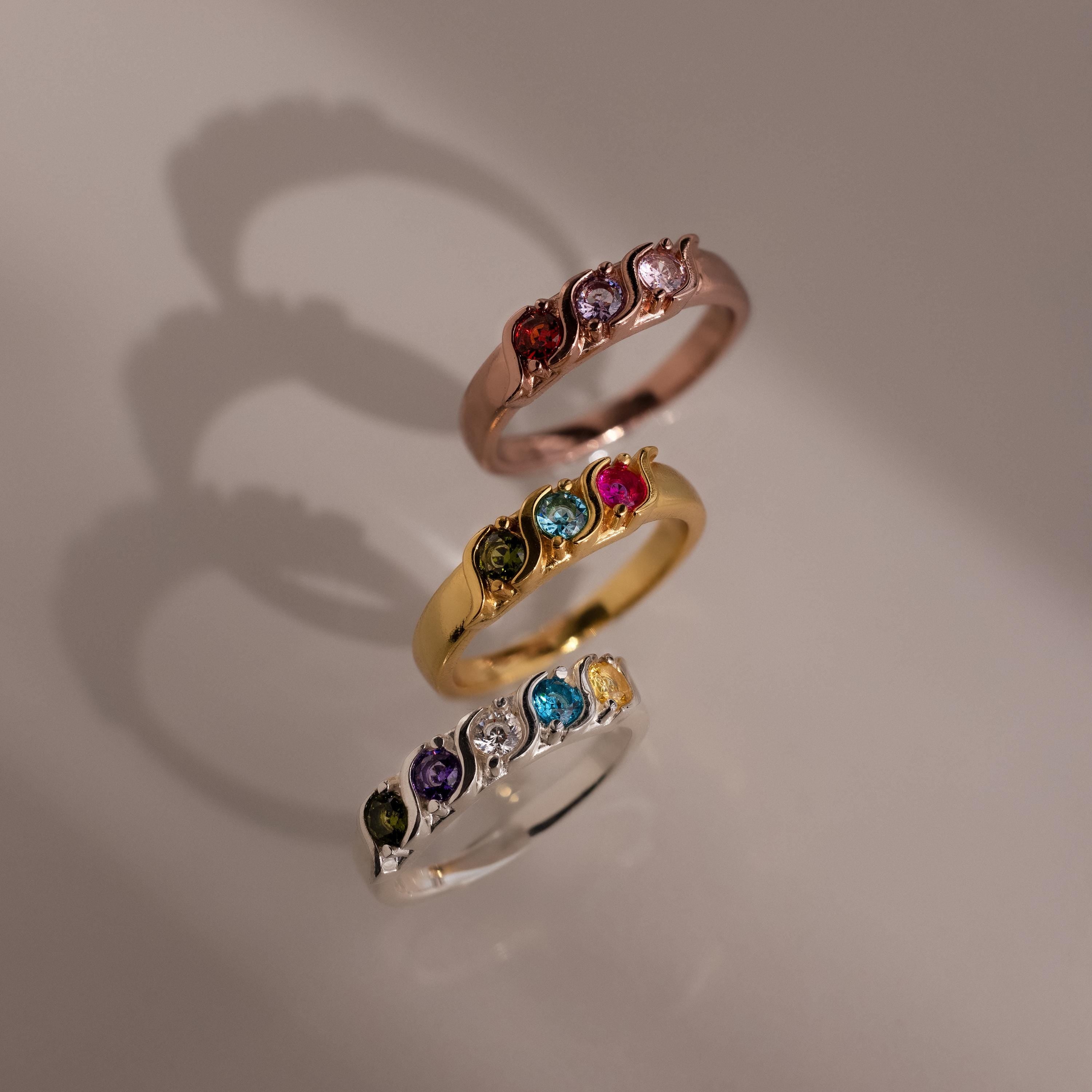 Three Vintage Multiple Birthstone Rings in rose gold, yellow gold, and silver shine with colorful stones on a neutral background.