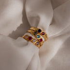 The Vintage Multiple Birthstone Ring, a gold ring featuring colorful gemstones and customized birthstones, displayed on soft, cream-colored fabric.