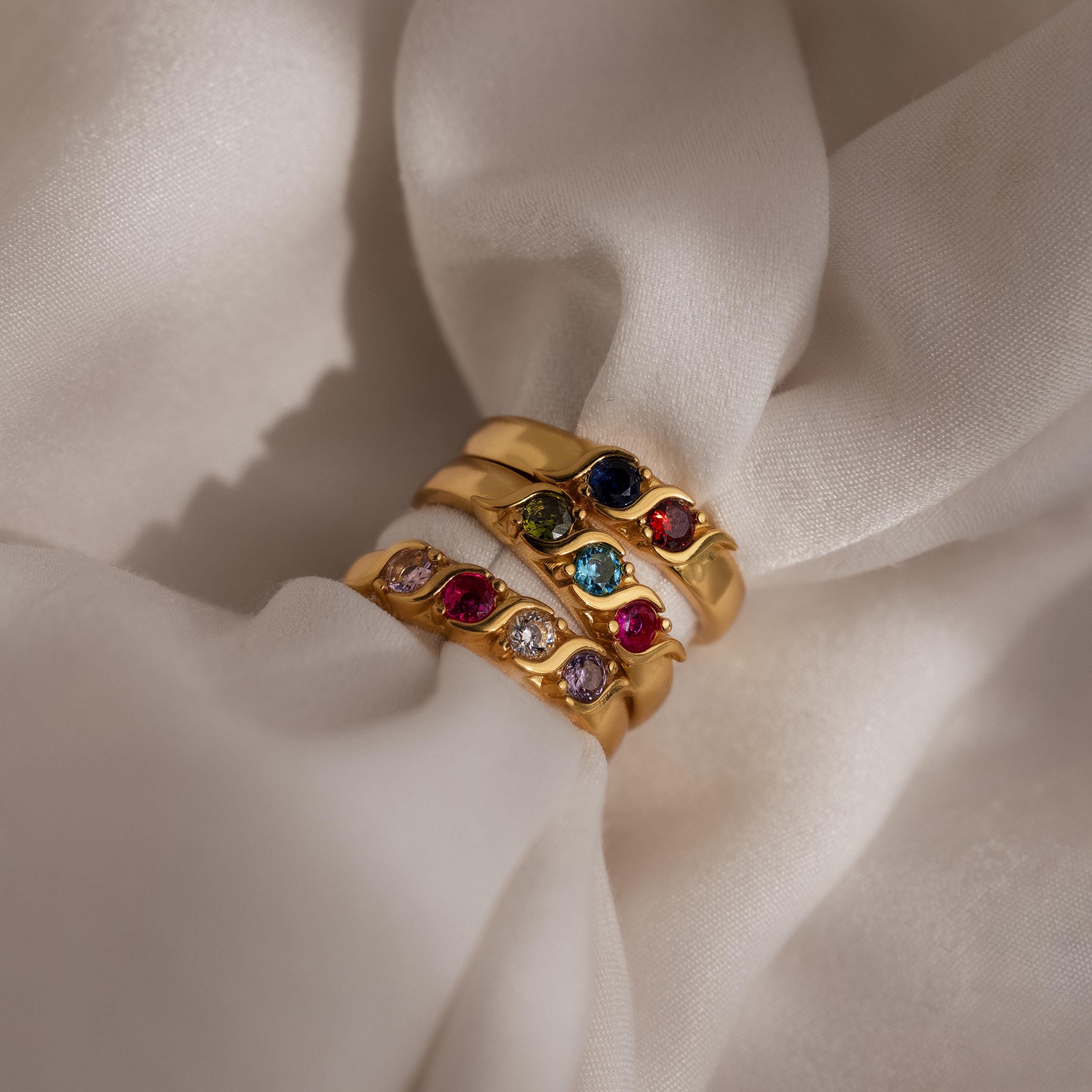 The Vintage Multiple Birthstone Ring, a gold ring featuring colorful gemstones and customized birthstones, displayed on soft, cream-colored fabric.