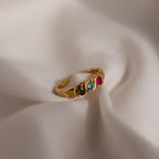 Vintage Multiple Birthstone Ring featuring four colorful gemstones displayed on soft, beige fabric.