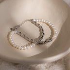 The Duo Beaded Pearl Bracelet, featuring delicate white pearls and silver beads, is elegantly displayed in a cream-colored dish.