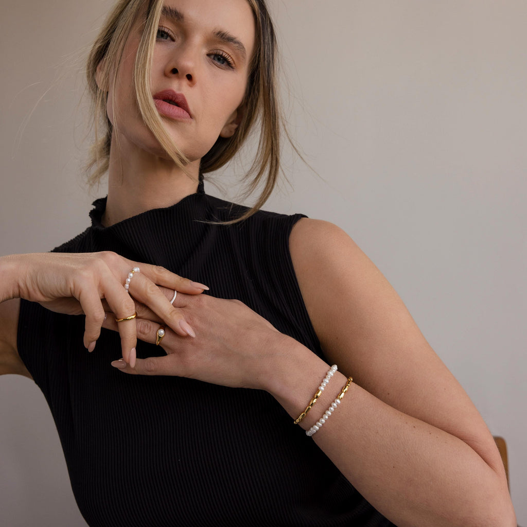 Woman wearing a sleeveless black top poses against a neutral background, styled with gold rings and the Duo Beaded Pearl Bracelet.