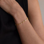 The Diamond Chain Tennis Bracelet, featuring gold links and round clear stones, is worn elegantly with a sleeveless black top.