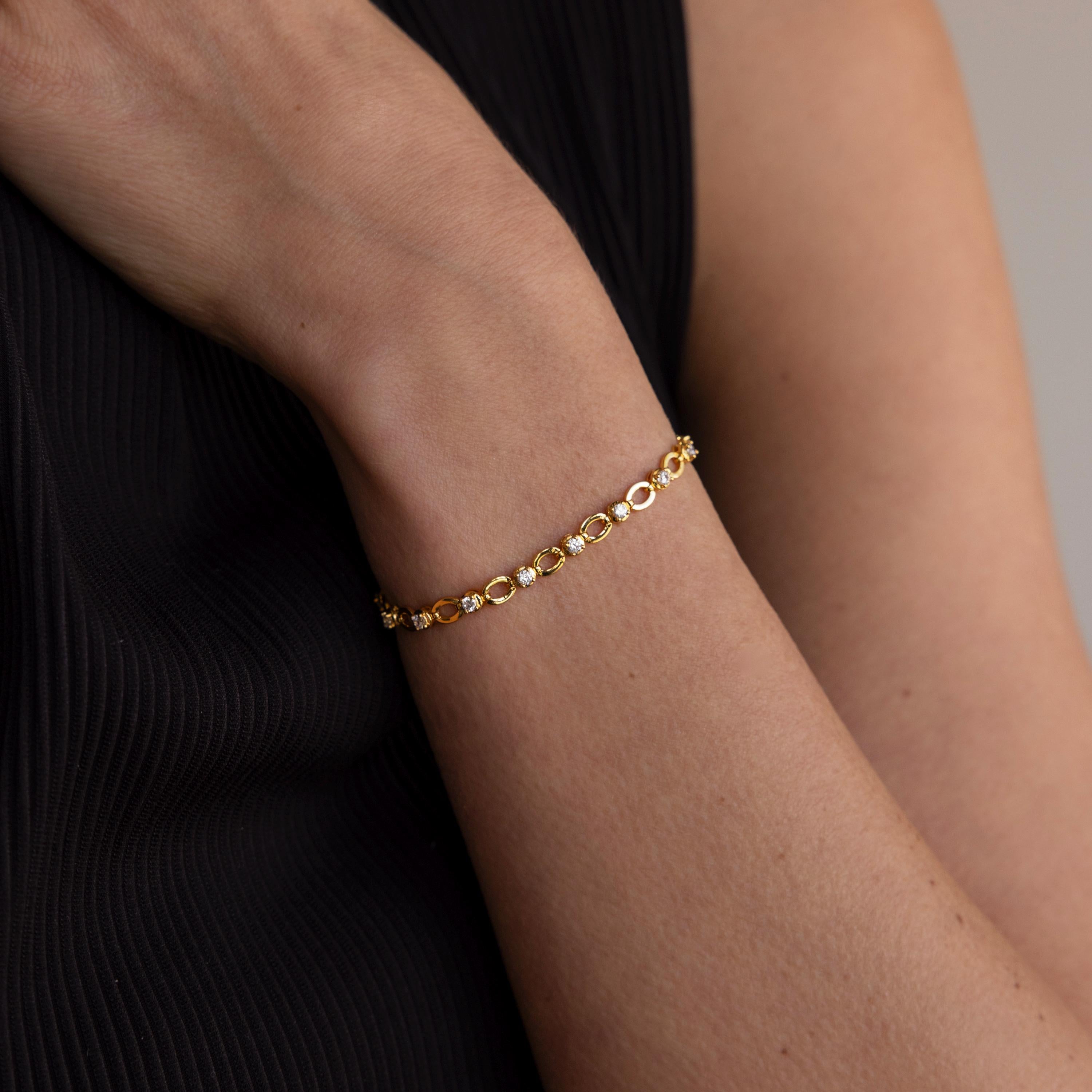 The Diamond Chain Tennis Bracelet, featuring gold links and round clear stones, is worn elegantly with a sleeveless black top.