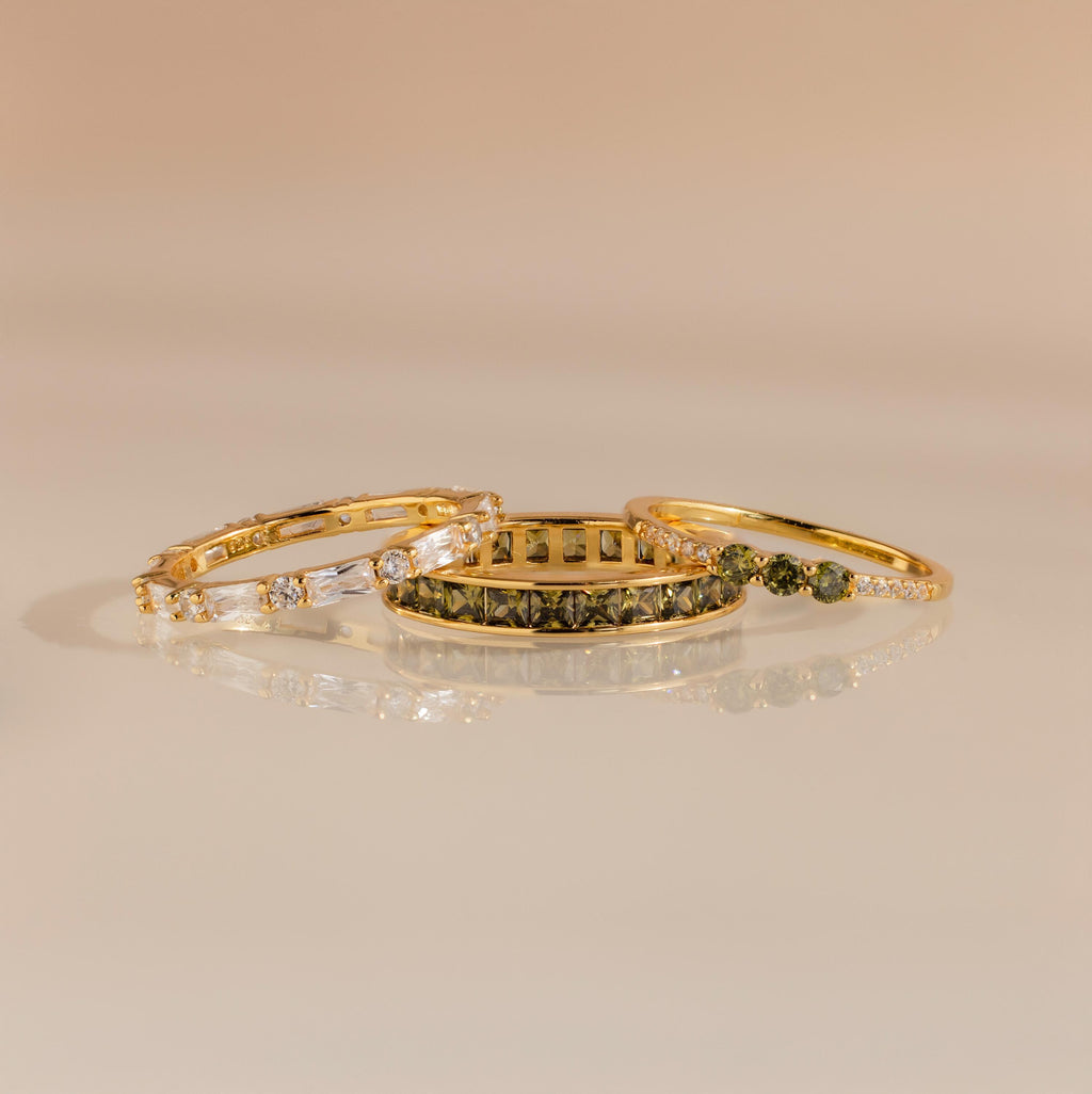 Three gold rings displayed flat with peridot and diamond designs, arranged side by side.