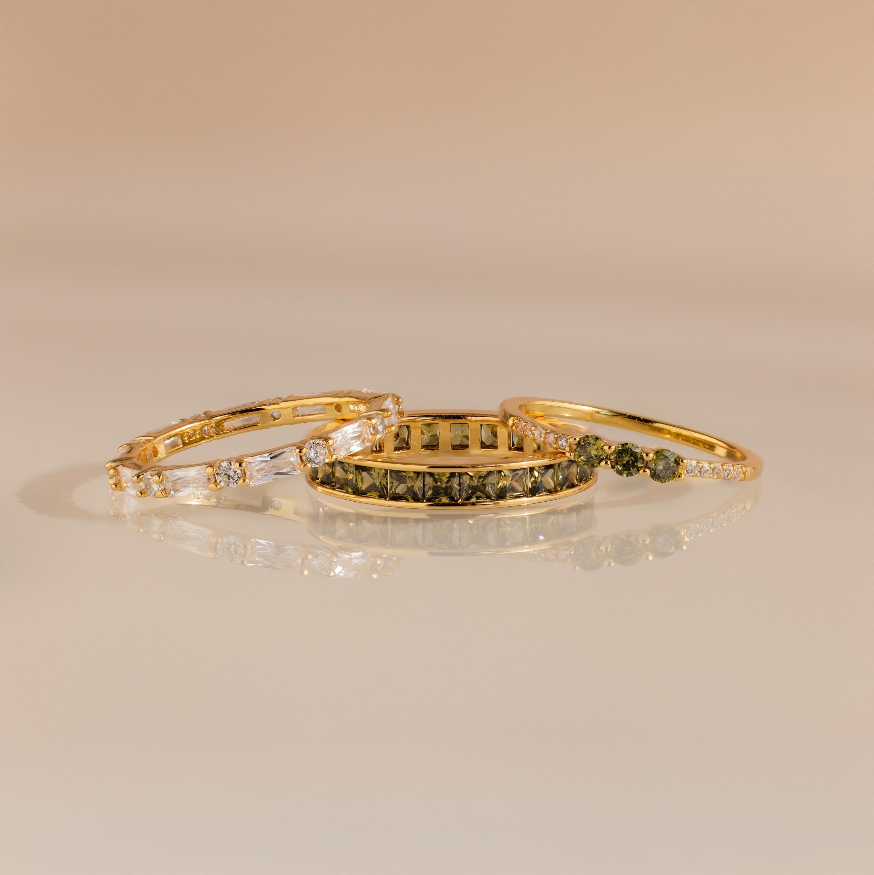 Three gold rings displayed flat with peridot and diamond designs, arranged side by side.
