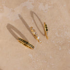 Overhead view of three gold peridot and diamond rings casting shadows on a beige surface.