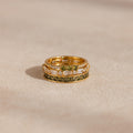 Close-up of three stacked gold peridot and diamond rings placed on a neutral fabric surface.