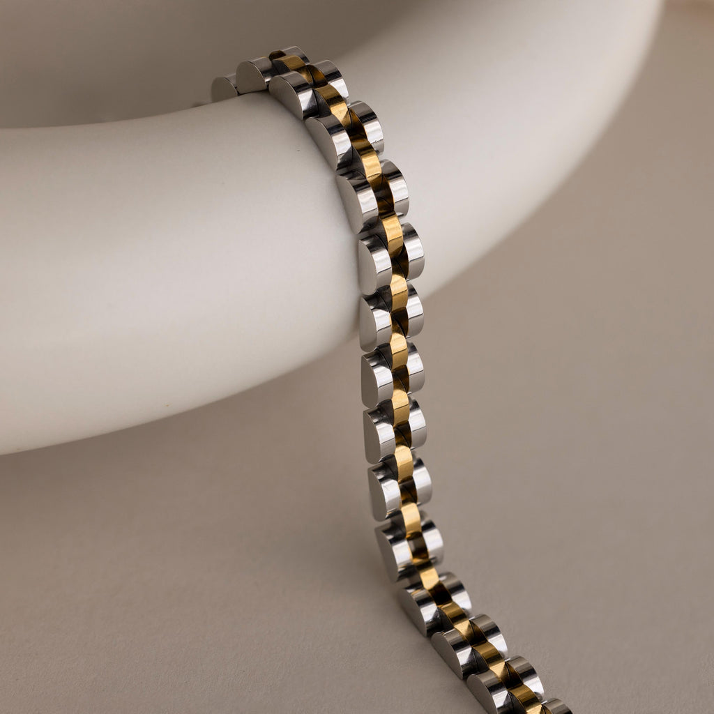 The Mixed Metal Link Bracelet features gold and silver links draped over a smooth white surface—a striking accessory that makes an ideal gift for him.