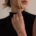 A woman in a black top wears the Pearl Hand Chain Bracelet adorned with small pearls, gently touching her chin—the perfect accessory for summer elegance.