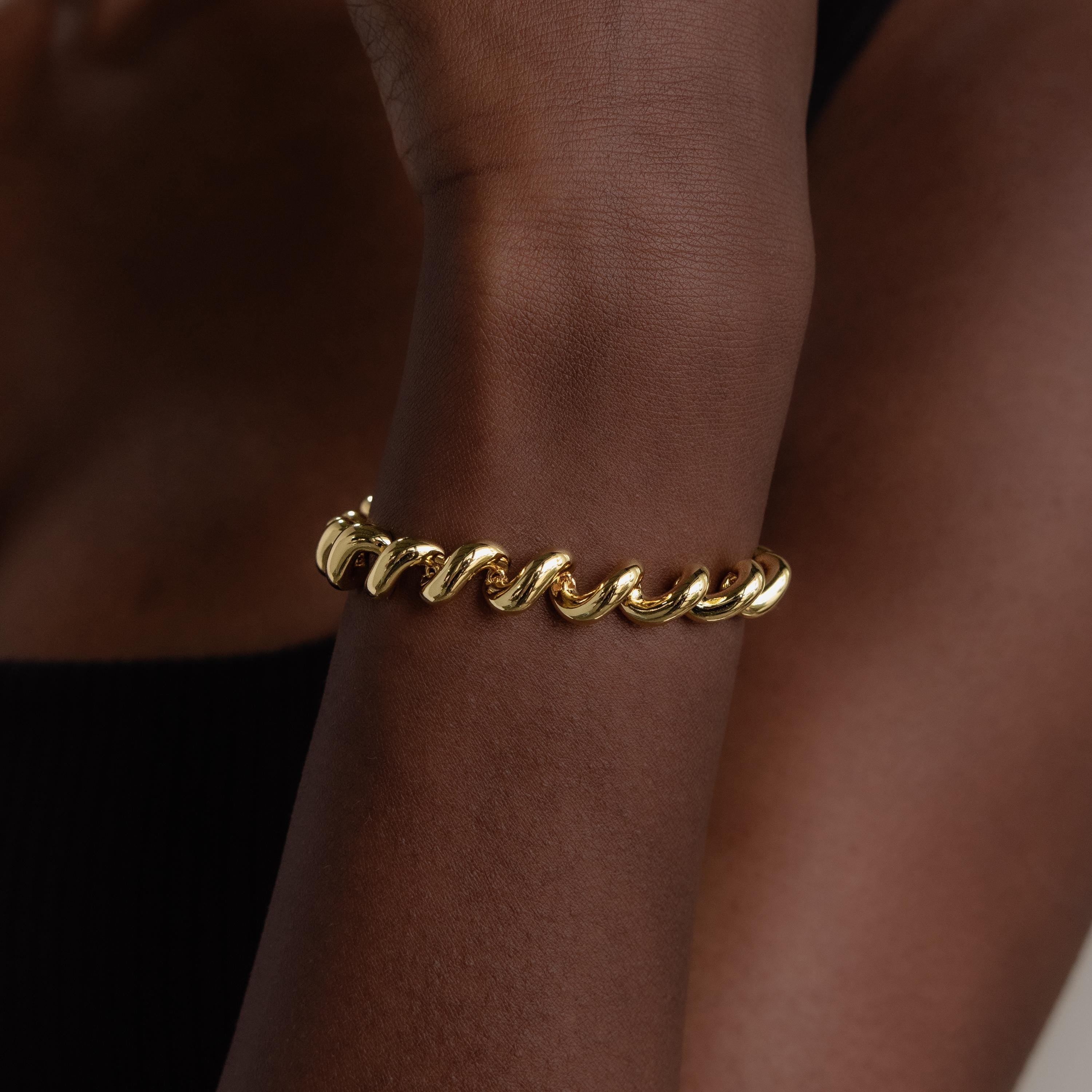 The Twisted Chain Bracelet features bold, shining links that wrap effortlessly around your wrist, exuding glamour against a dark background.