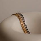 A V-Link Chain Tennis Bracelet with sculptural links is elegantly draped over a smooth, curved beige surface.