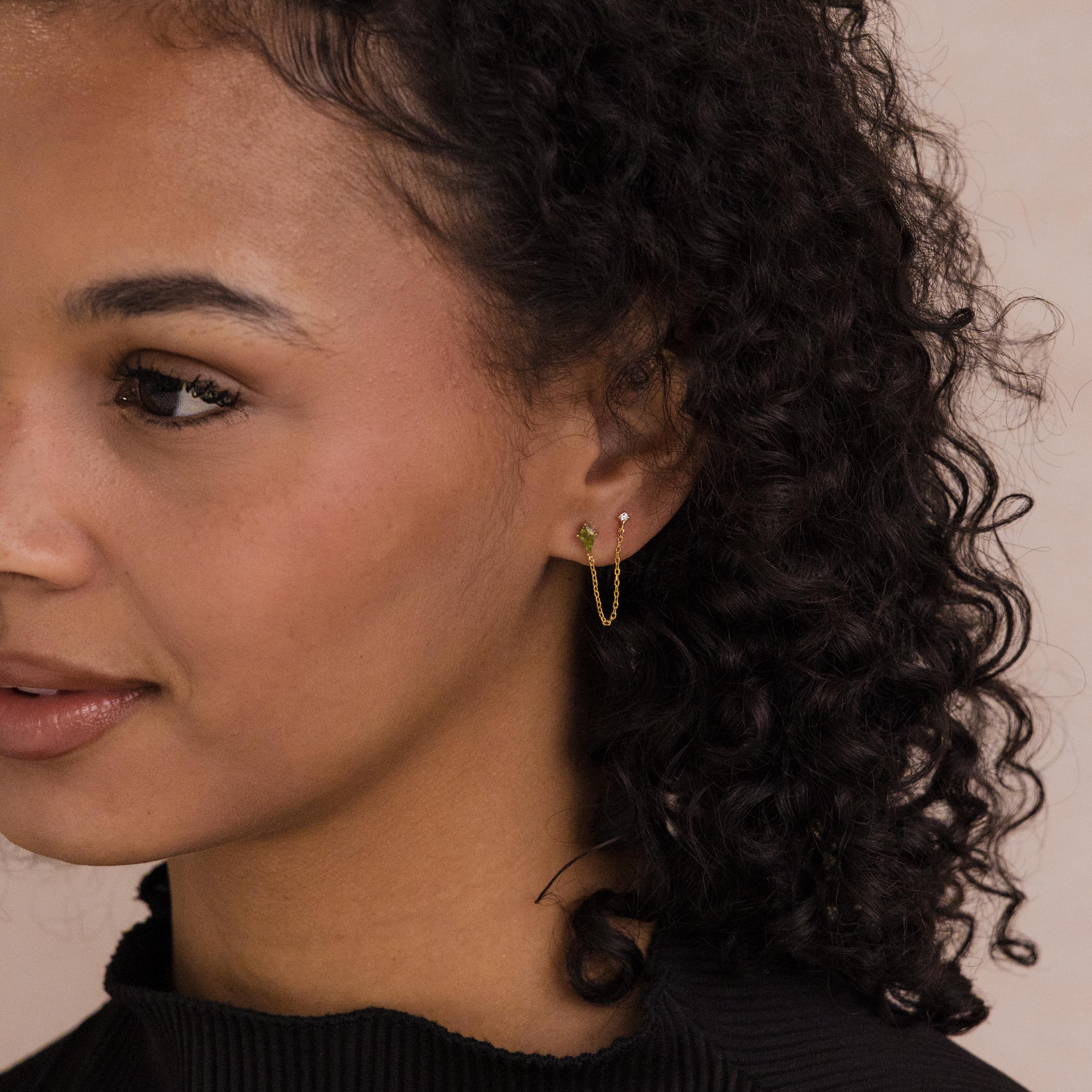 A woman with curly hair, wearing a black top and the Agate Diamond Chain Earrings, looks to the left.