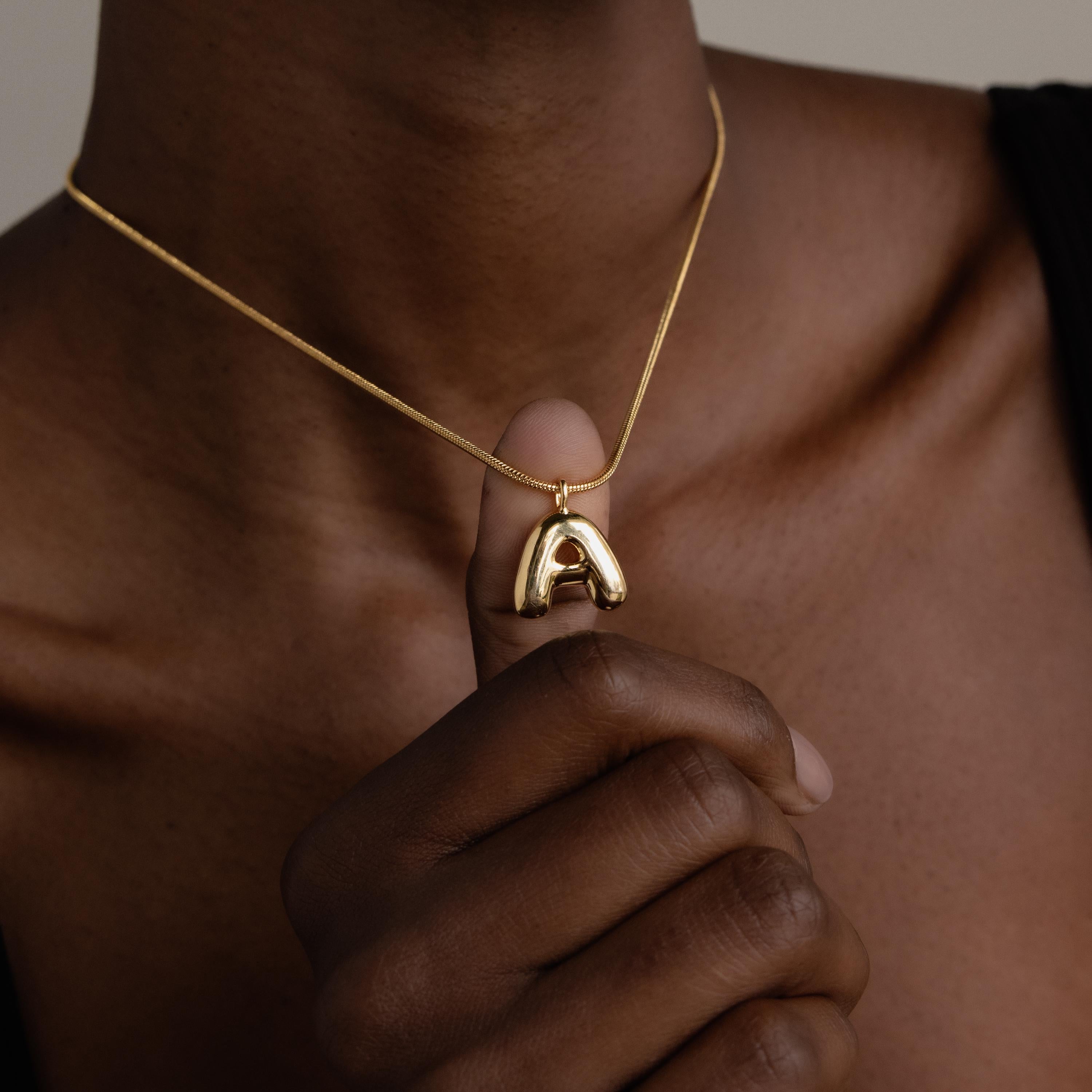 A person holds a Bubble Letter Necklace with a large gold A pendant against their chest, showcasing stylish personalized jewelry.