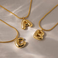 The Bubble Letter Necklace in 18K Gold features glossy, chunky letter charms A, B, and C arranged on a light surface with soft shadows—ideal for fans of personalized jewelry.