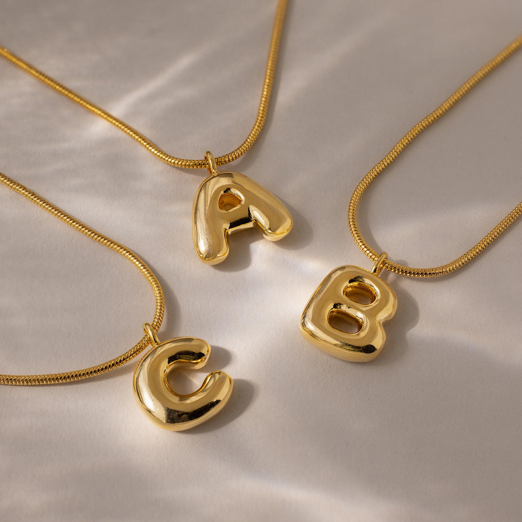 Three gold Bubble Letter Necklaces, each with a shiny, chunky A, B, or C pendant, displayed on a light surface—ideal personalized jewelry or standout charm necklaces for any occasion.