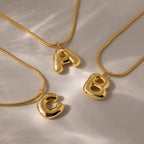 Three gold Bubble Letter Necklaces, each with a shiny, chunky A, B, or C pendant, displayed on a light surface—ideal personalized jewelry or standout charm necklaces for any occasion.