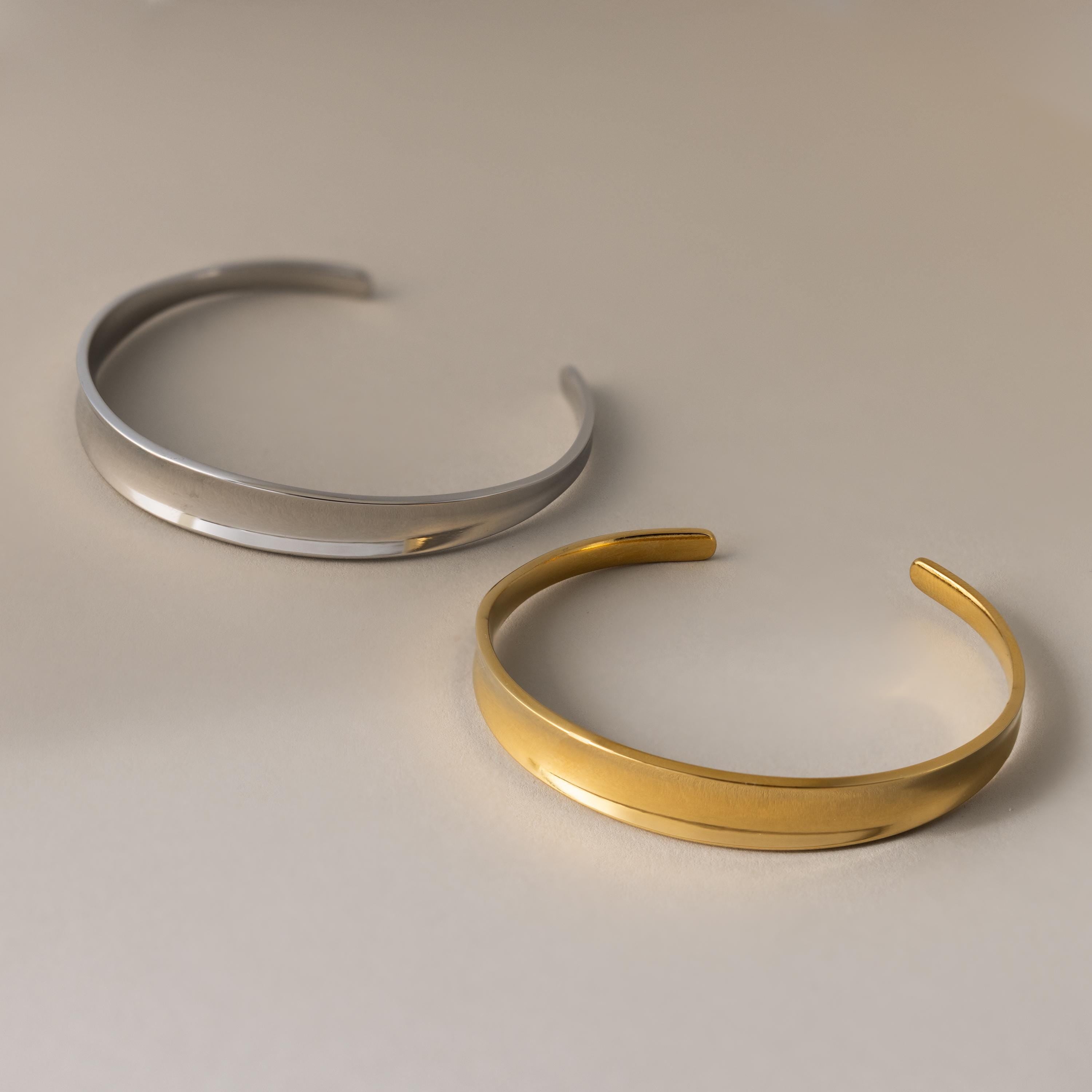 Two Dome Cuff Bracelets—one in silver and one in gold—add a stylish accent to any neutral backdrop.