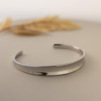 The Dome Cuff Bracelet is shown on a neutral surface with dried grass in the background, highlighting its minimalist design and making it a chic, stylish accent for any outfit.