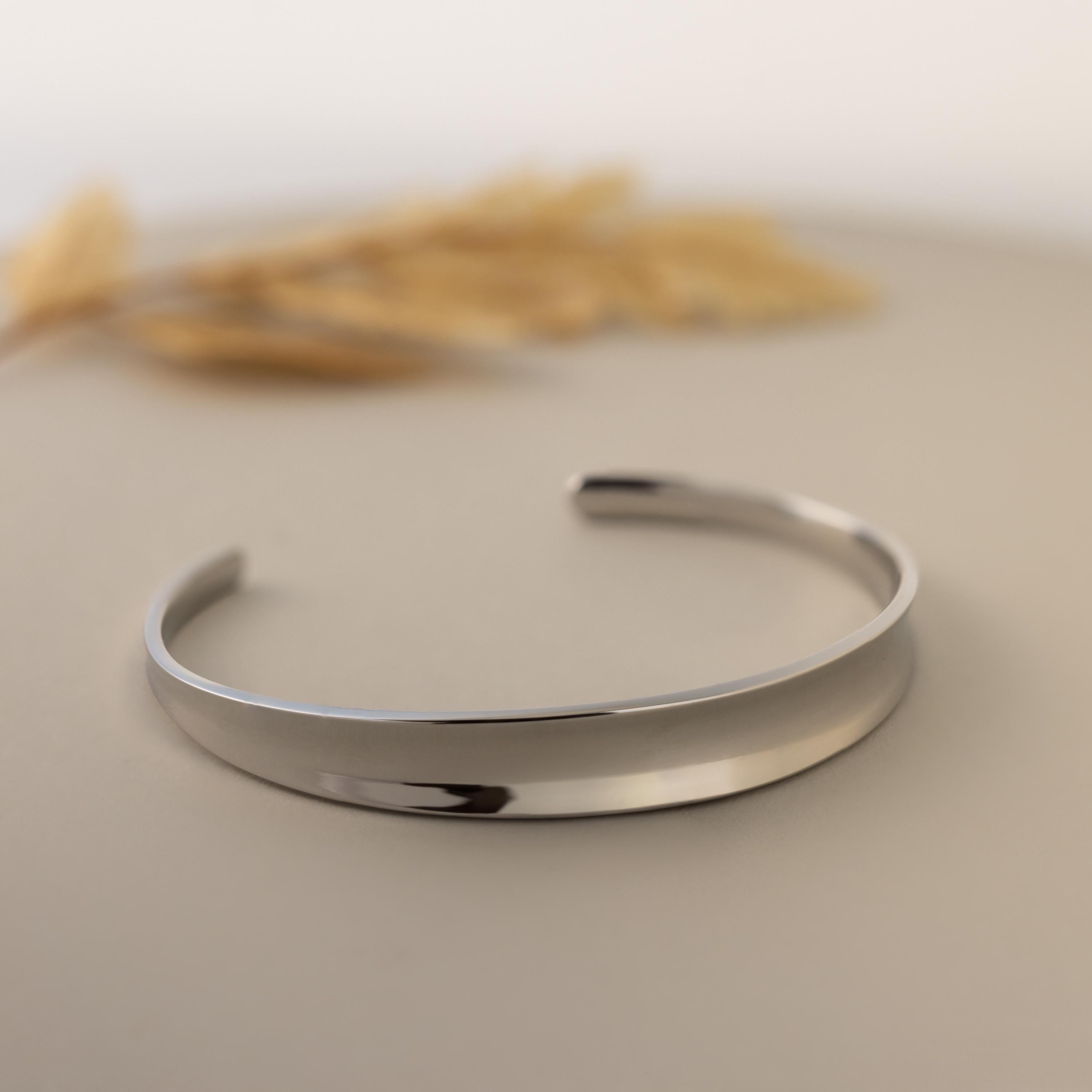 The Dome Cuff Bracelet is shown on a neutral surface with dried grass in the background, highlighting its minimalist design and making it a chic, stylish accent for any outfit.