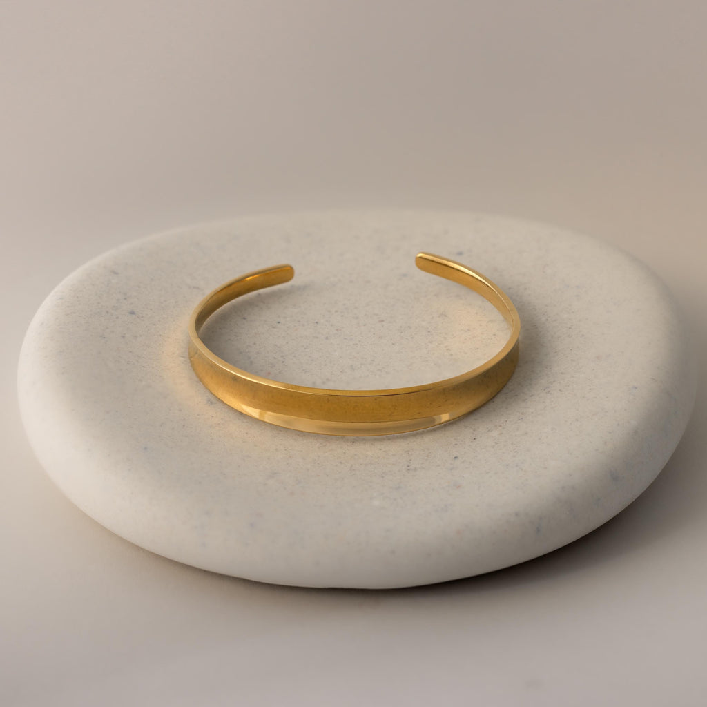 The Dome Cuff Bracelet is displayed on a round, smooth, light stone surface for a modern, stylish accent.
