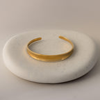 The Dome Cuff Bracelet is displayed on a round, smooth, light stone surface for a modern, stylish accent.