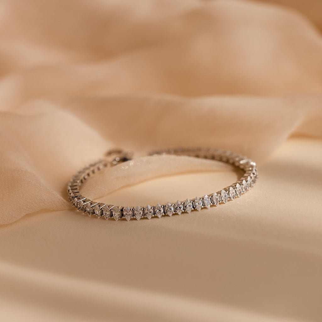 Close-up of the Marquise Diamond Tennis Bracelet in silver, featuring a continuous row of marquise-cut diamonds set in a sleek silver band, displayed on a soft beige fabric.