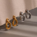 Two pairs of Bold Duo Knot Earrings, in gold and silver, rest on a beige textured surface. These sculptural earrings offer a modern update to your jewelry collection.