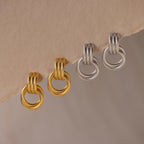 The Ribbed Duo Knot Earrings, featuring a textured hoop design in gold and silver, are displayed on a beige surface—perfect statement earrings for any occasion.