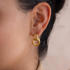 A close-up of a woman's ear showcases Ribbed Duo Knot Earrings—textured gold hoops that create an elegant statement look.