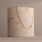 The Bold Paperclip Chain Necklace features rectangular links draped over a textured, cylindrical beige stone—a striking statement piece for any look.