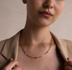 A woman holds the lapels of her beige blazer near her collarbone, showcasing the Bold Paperclip Chain Necklace.