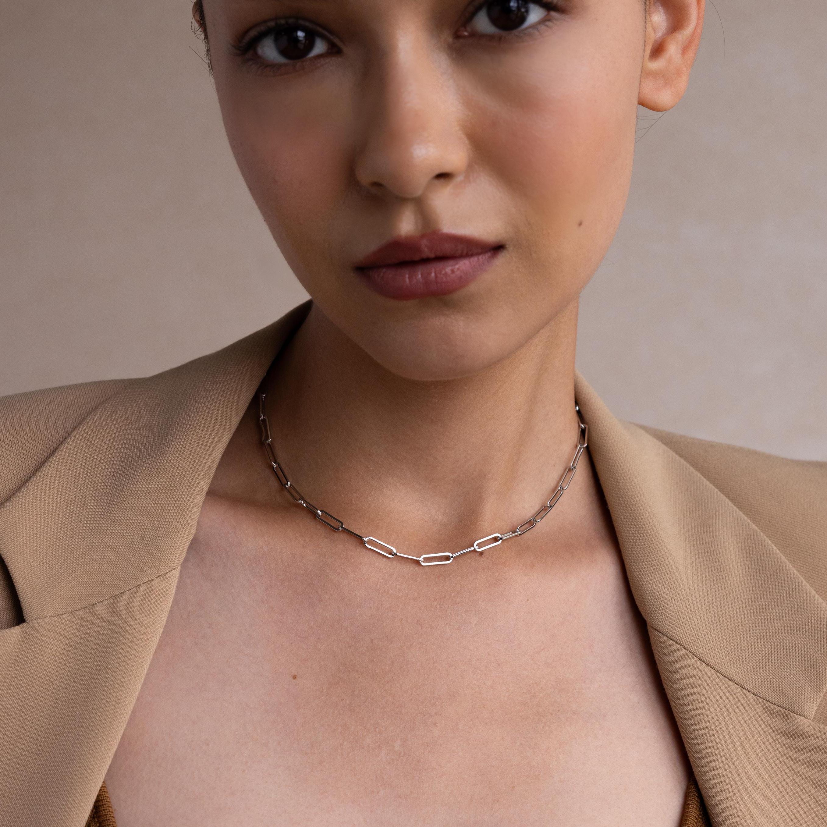 A woman wearing a tan blazer styles the Bold Paperclip Chain Necklace, looking at the camera with a neutral expression.