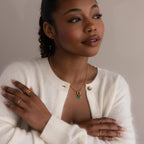 Model wears gold rolo circle necklace with multiple emerald-colored birthstone charms. She completes the look with golden rings.