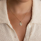 A person wearing a cream textured button-up shirt showcases the Pearl Flower Birthstone Necklace, featuring a gold 925 sterling silver chain and oval mother of pearl pendant, with focus on the necklace and upper chest area.